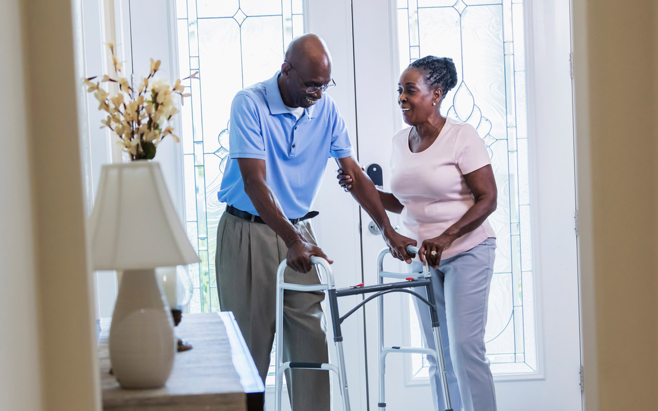 Photo of senior man with a walker, and his wife at a door